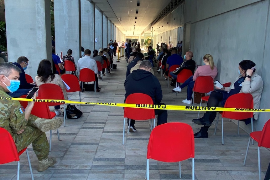 People sit in chairs socially distanced from each other outside a vaccine centre.