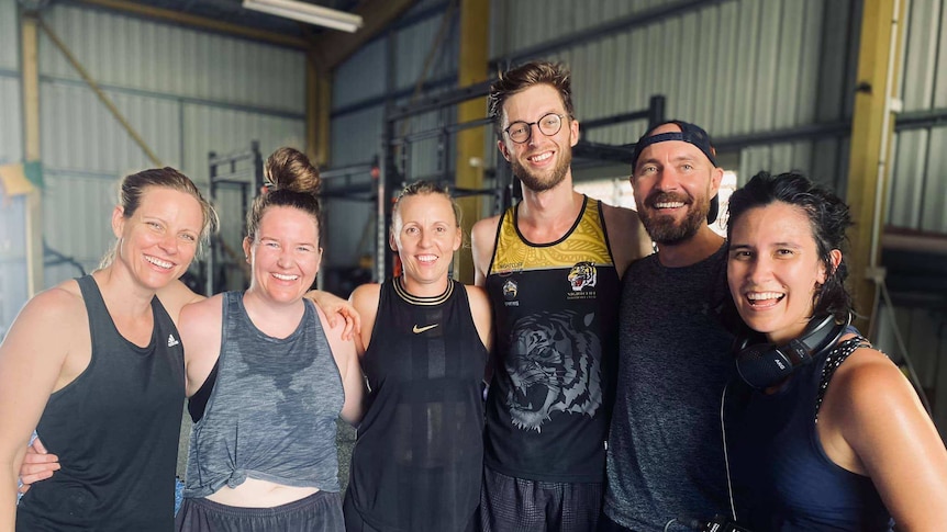 4 women and two men smiling at the camera in a gym