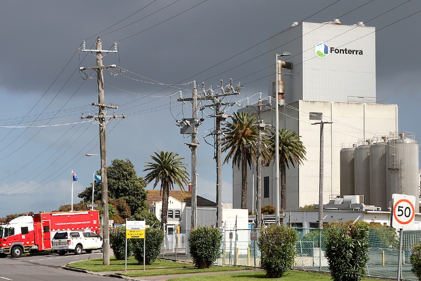 A large concrete building with Fonterra sign and cylinder vats on a street with cars in the driveway.