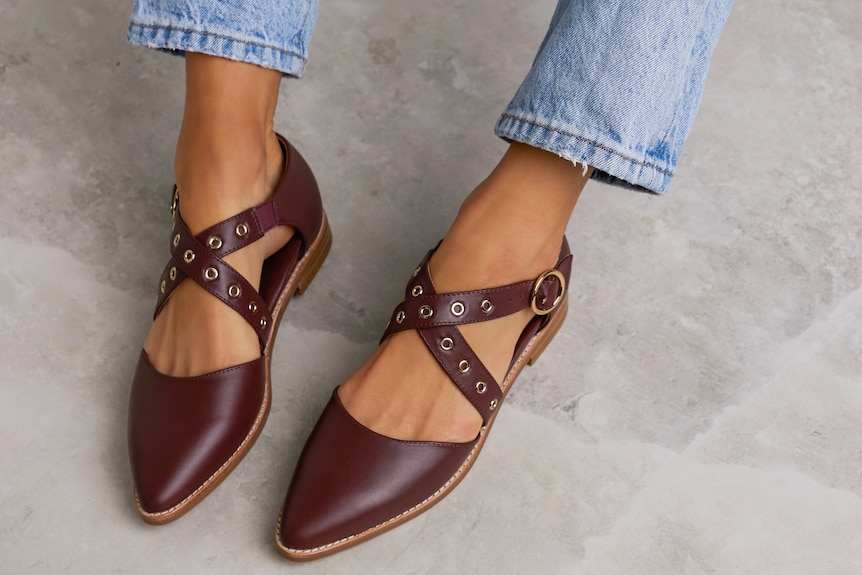 A pair of burgundy leather shoes, modelled by a woman.