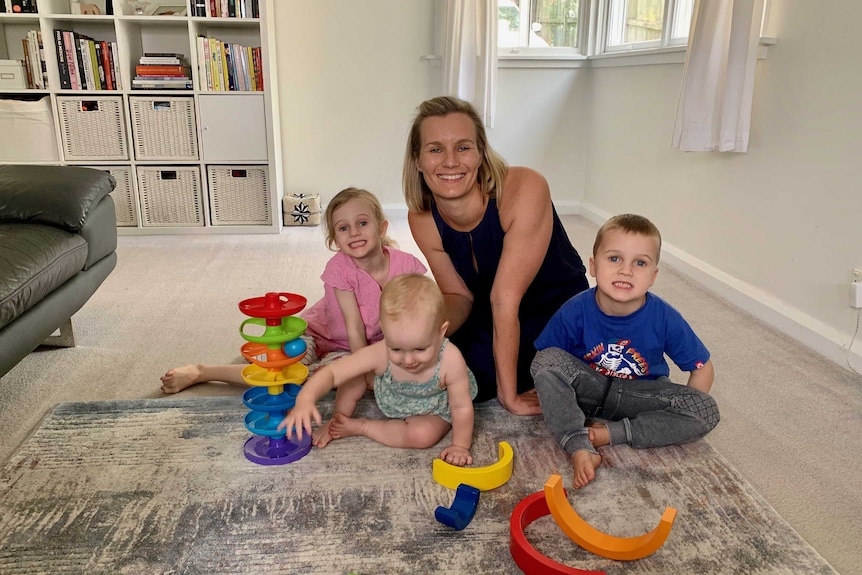 Erin Remblance and her three young children posing for a photo graph sitting on their lounge room floor with some baby toys