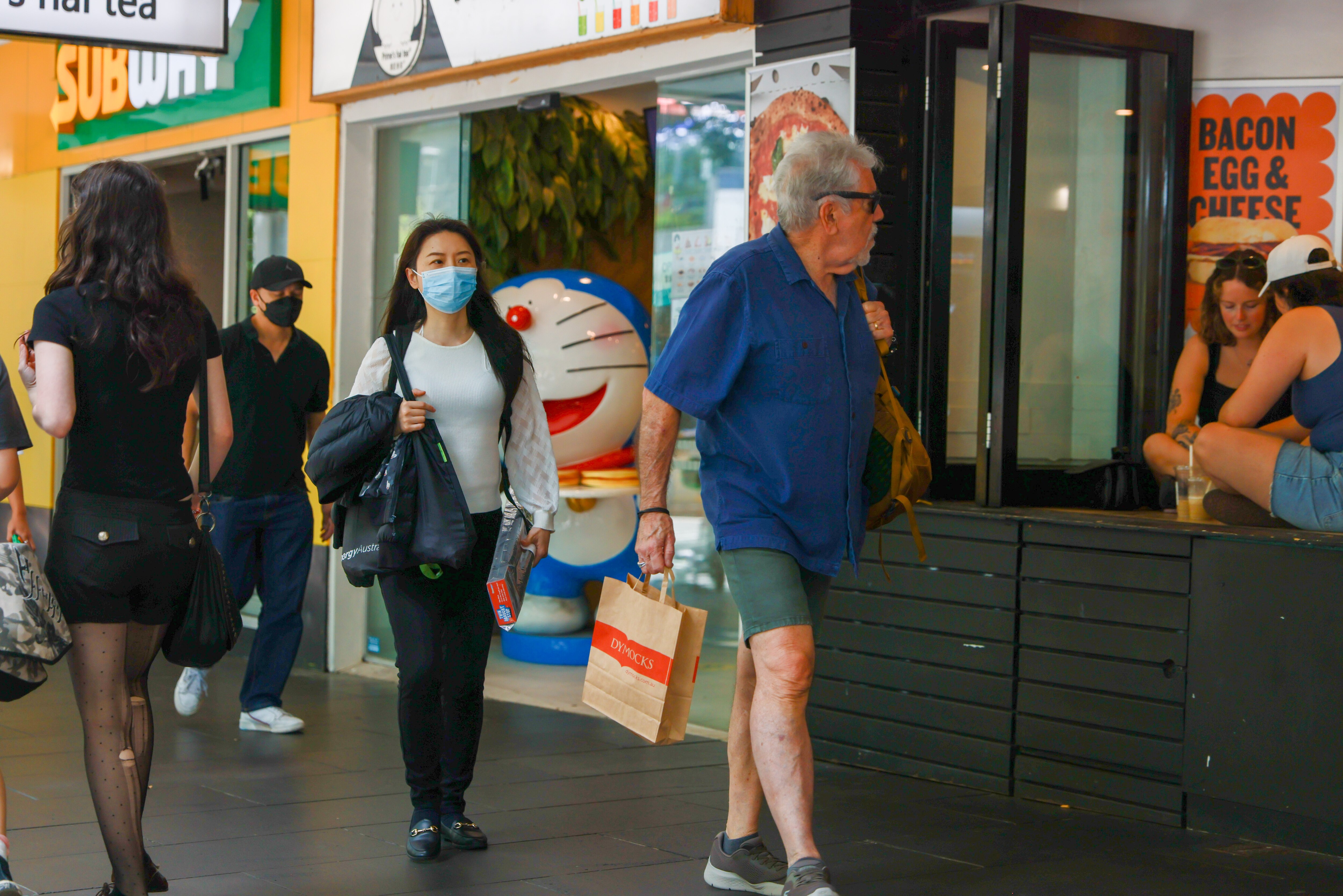 Faded social distance stickers on the footpath and people walking with masks as they pass hand sanitiser stations.