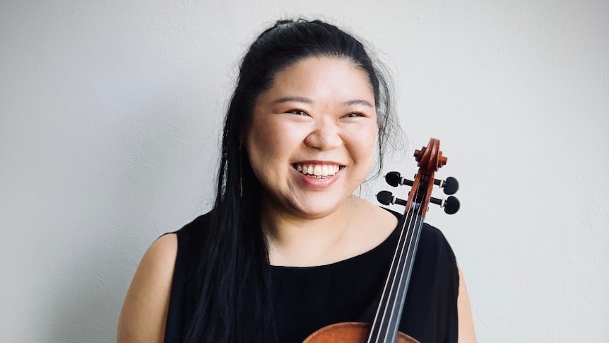 Eunise Chen stands holding her viola in front of a white backdrop.