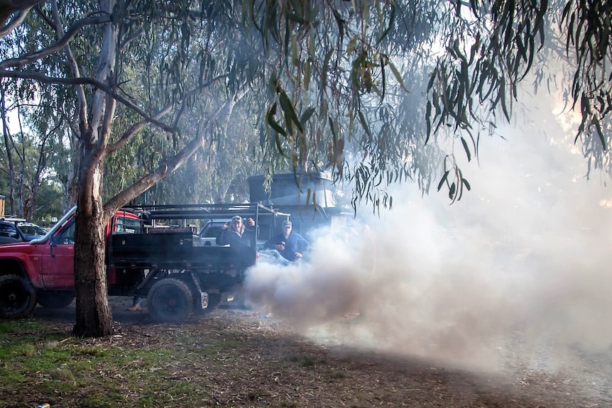 A red ute with a black tray leaves a cloud of smoke as it revs at B and S ball.