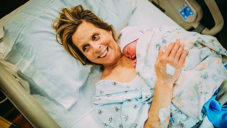 Cecile Eledge smiles lying on a hospital bed cradling her grandchild she gave birth to.