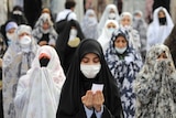 Women wear protective face masks and gloves as they pray in a mosque courtyard.
