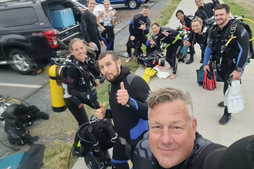 people in scuba diving gear smiling and waving