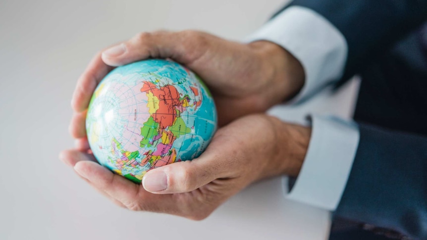A person in a suit cradles a miniature globe in their hands