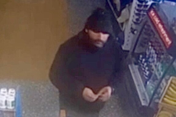 A man wearing black clothing and a black beanie on CCTV footage. 