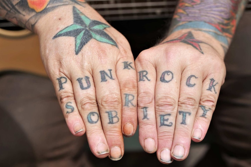 A pair of hands with the words "punk rock" and "sobriety" tattooed across the fingers.