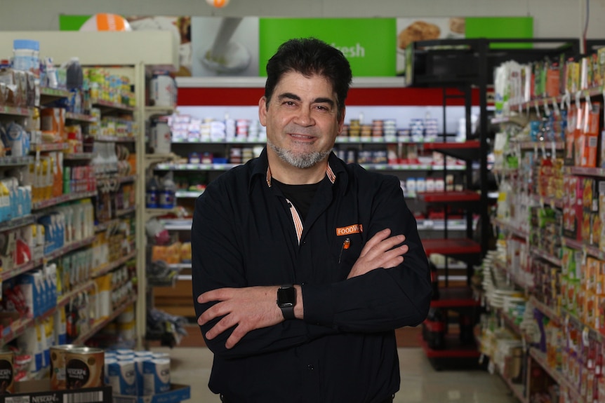 A man stands in a supermarket aisle and folds his arms