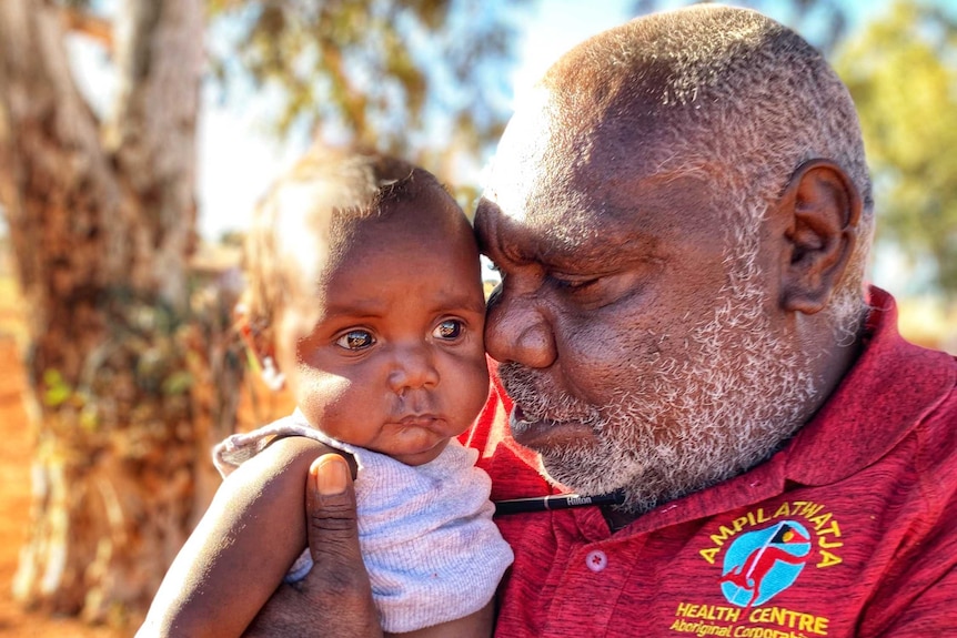 A man holds a baby wearing a singlet and nappy.