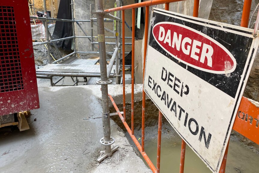 Sign warns of "danger- deep excavation" at a construction site.