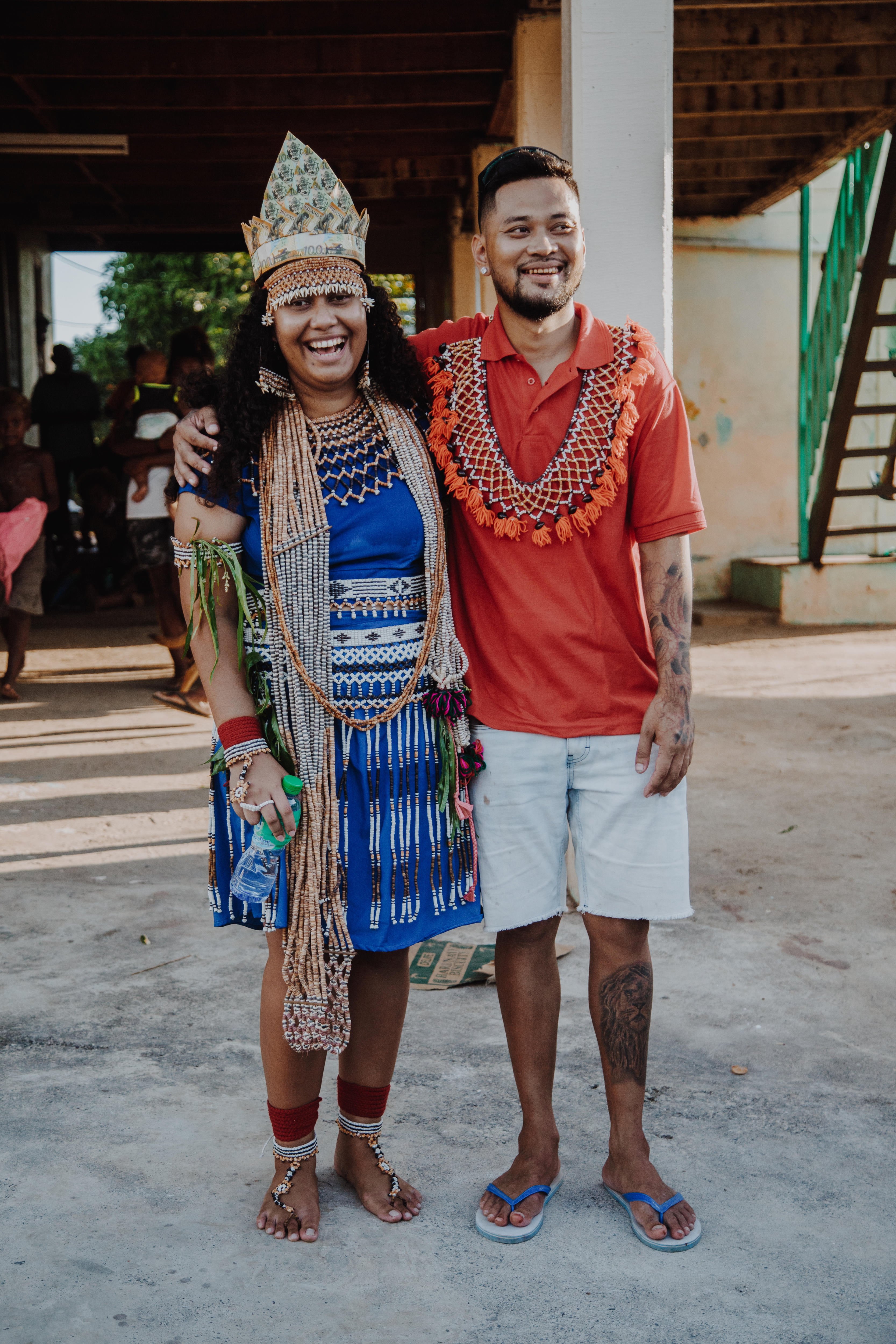 A bride and groom stand together smiling at a bride price ceremony.