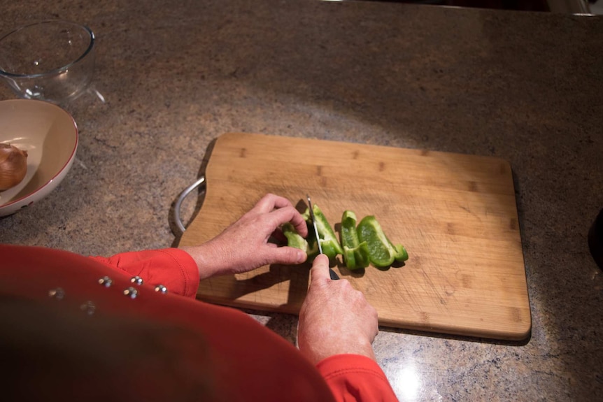 A woman chops a capsicum on a chopping board.