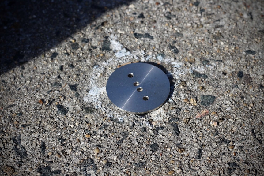 The circular silver rod is hammered into the cement path.