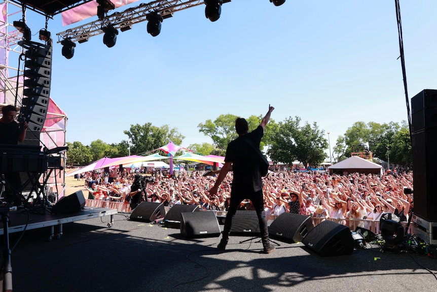 Musician Boo Seeka standing onstage at a music festival in front of a large crowd, with his back facing the camera and arms out.