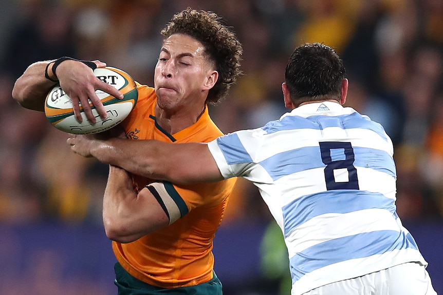 A Wallabies player holds the ball as he is tackled around is chest by a Pumas' opponent.