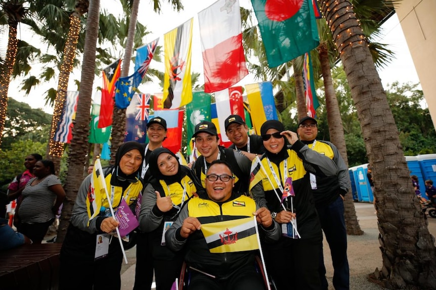 A team of smiling people stand under flags.
