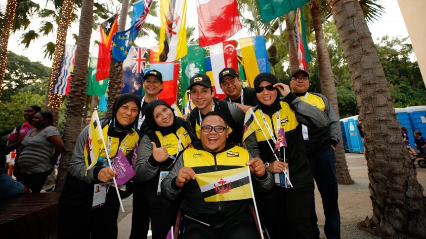 A team of smiling people stand under flags.
