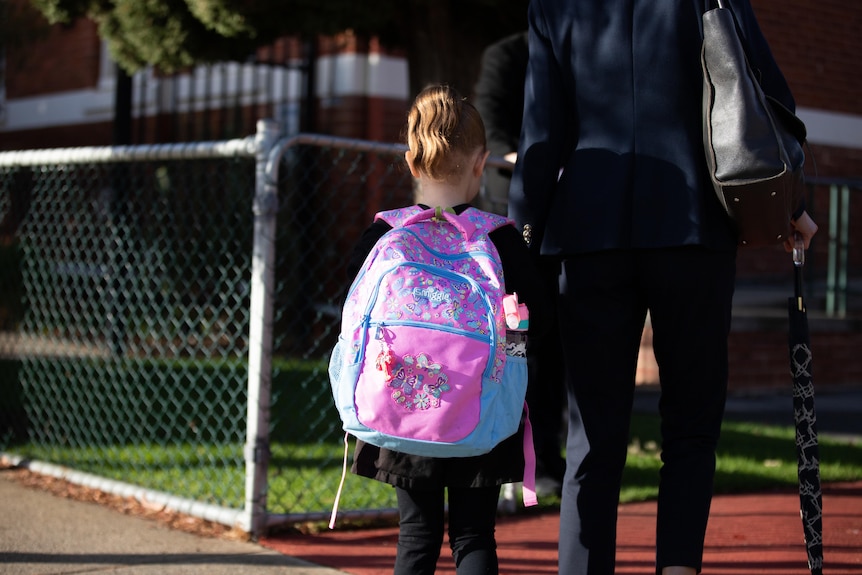 Girl with pink schoolbag walks with her mum to school.