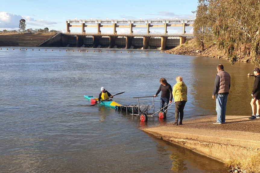 Two people lower a canoe into water at a boat ramp while two other people look on