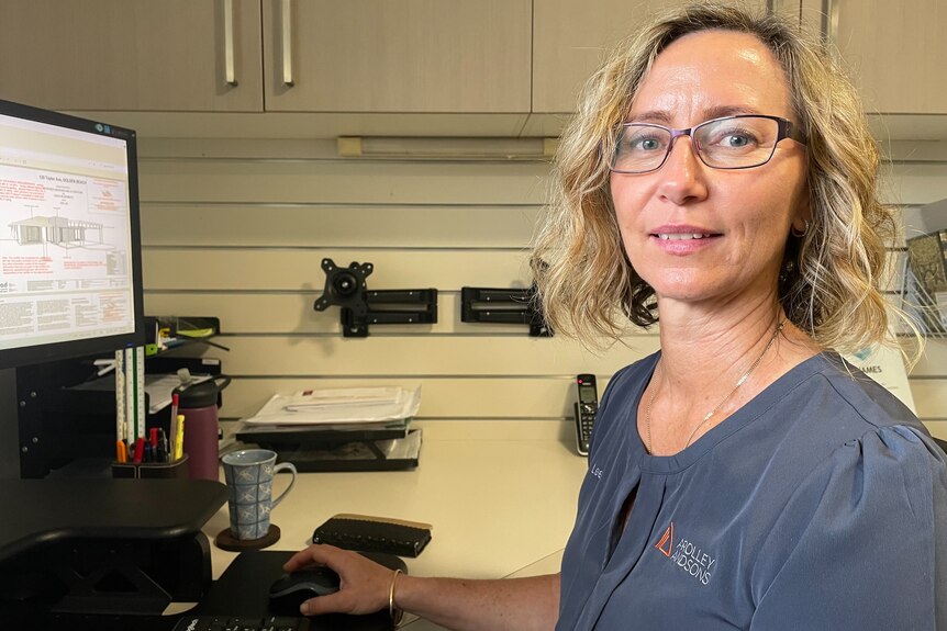 Une femme aux cheveux blonds mi-longs et portant des lunettes utilise un ordinateur