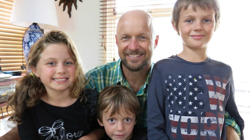 A man with a slight beard with his two sons and daughter, all smiling