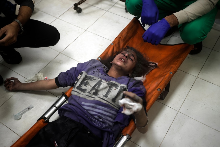 A girl lying on an orange stretcher while holding one hand up.