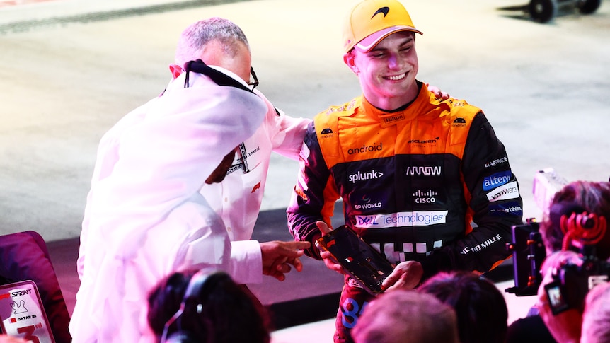 An F1 driver, out of his car, surrounded by pit in the pit, being congratulated