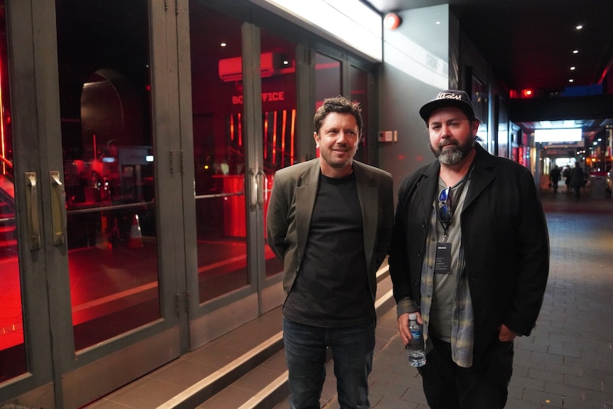 Two men stand outside a theatre at night