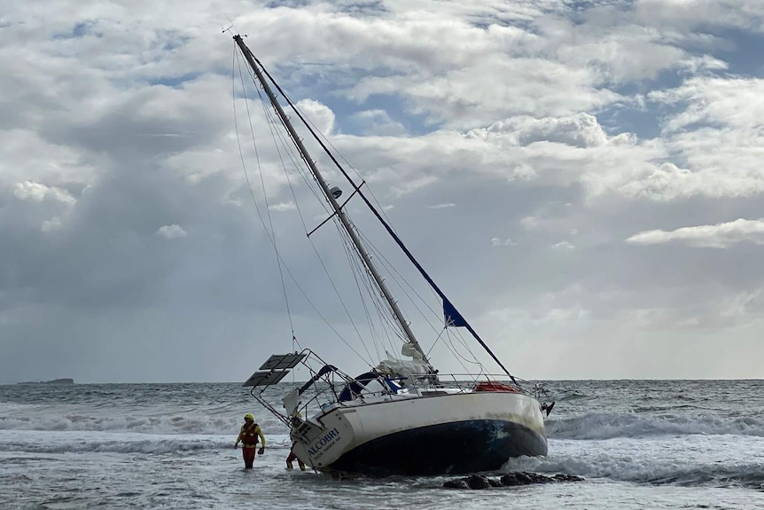 A rescue worker in the water beside a yacht washed up on a beach