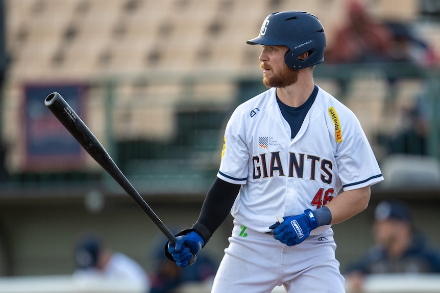 A baseball batter holding a bat with the word GIANTS on the front of his shirt