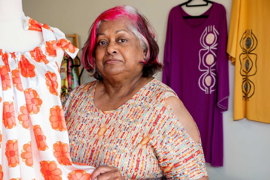 A woman stands with a dress in a clothing store.