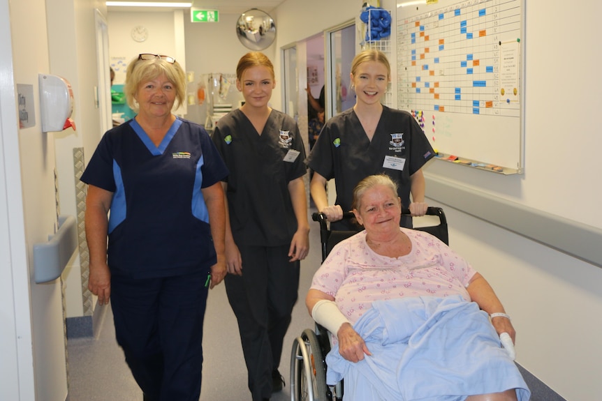 three women standing with a hospital patient in a wheel chair and bandages on her hands