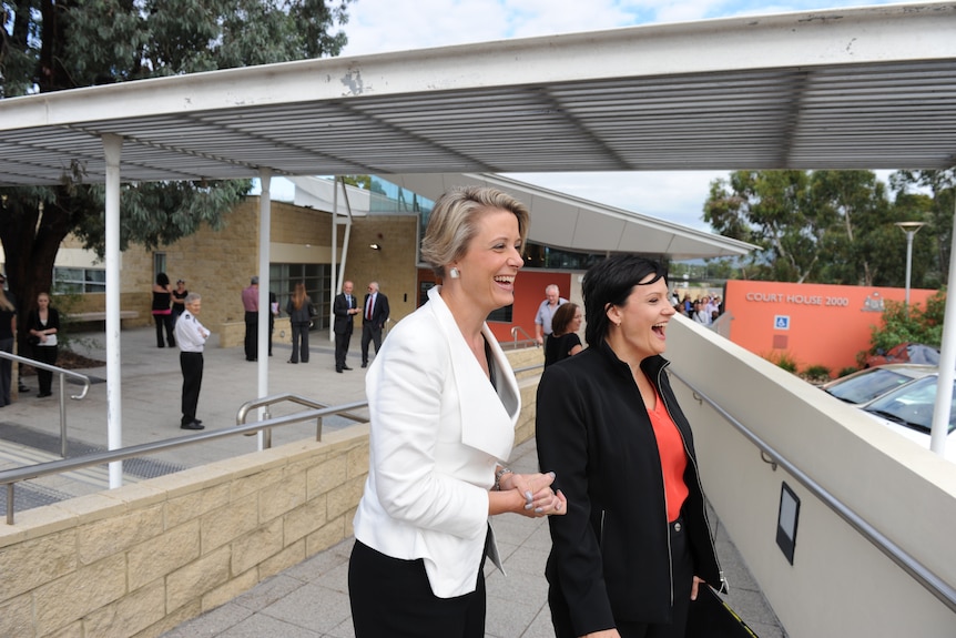 Women wearing white and black jackets laugh.