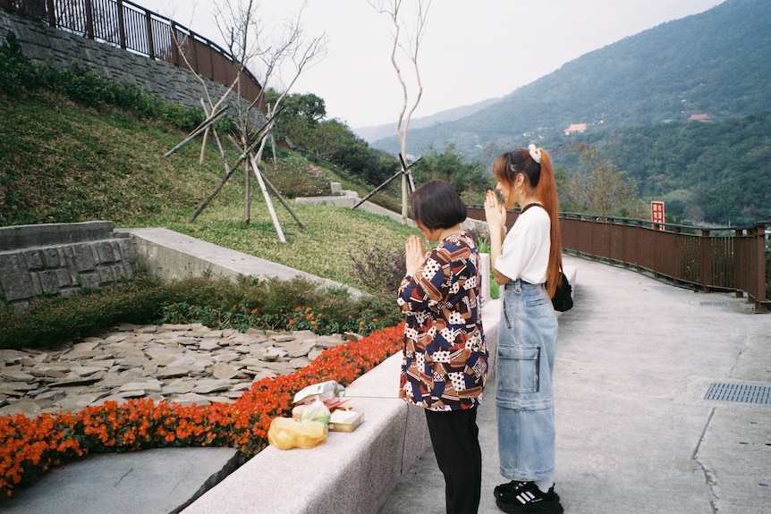 A middle-aged Taiwanese woman in a colourful print shirt and a young Taiwanese woman in a white shirt and jeans pray at a shrine
