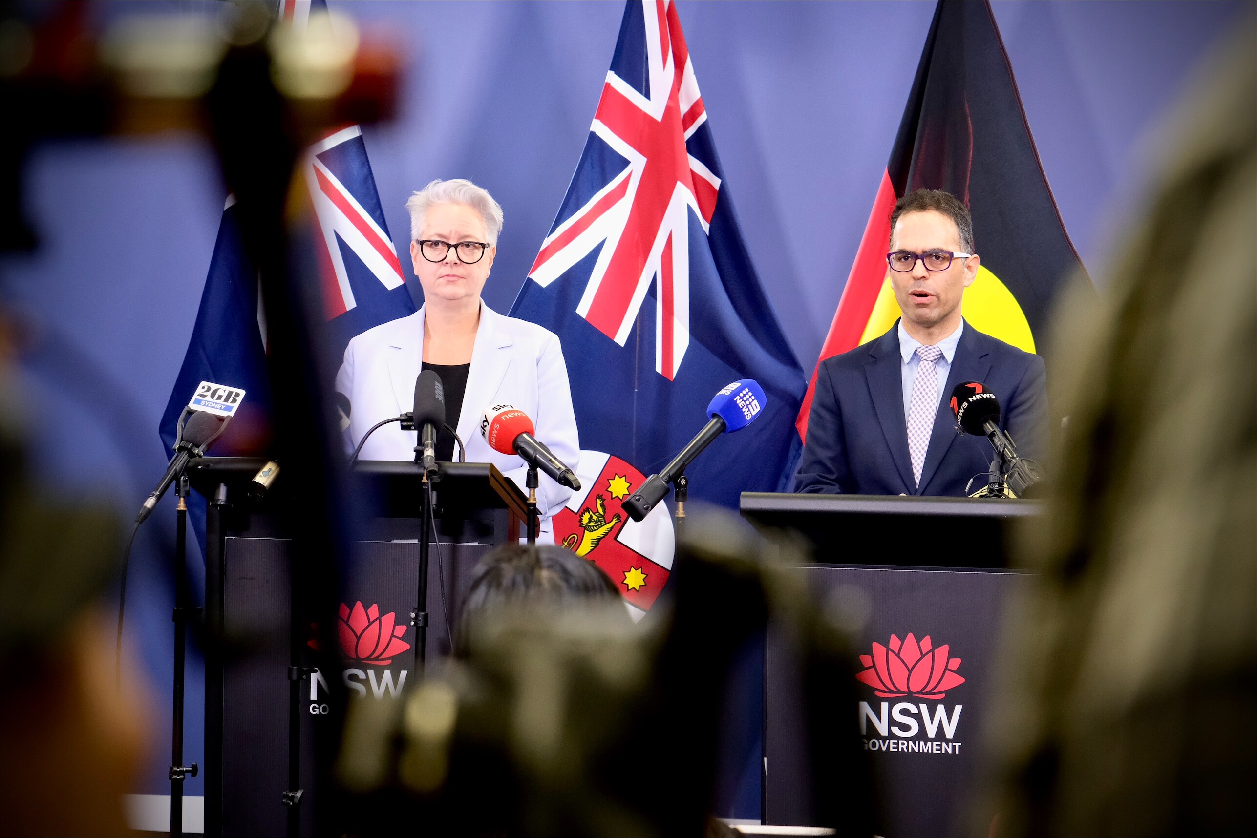 A man at a woman stand at a podium with microphones in front of them.