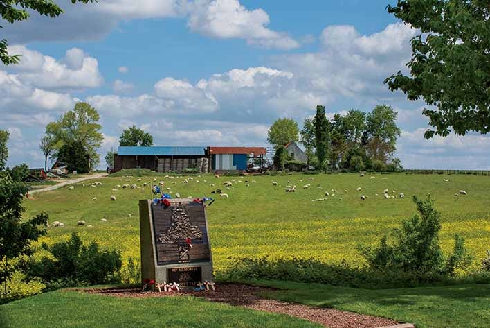 Farmhouse sitting on the top of a rise with a memorial in the foreground