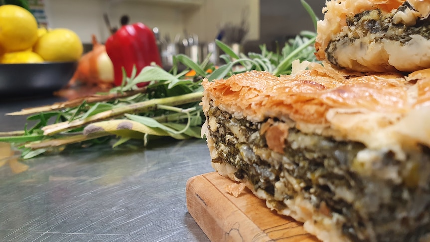 Two slices of cheese and leafy greens pie stacked on a chopping board, next to a sprig of leafy greens.