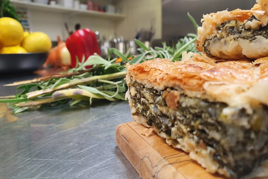Two slices of cheese and leafy greens pie stacked on a chopping board, next to a sprig of leafy greens.