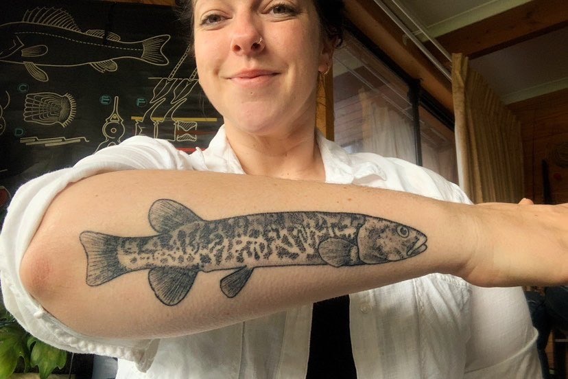 Smiling woman holds up arm tattooed with a large fish