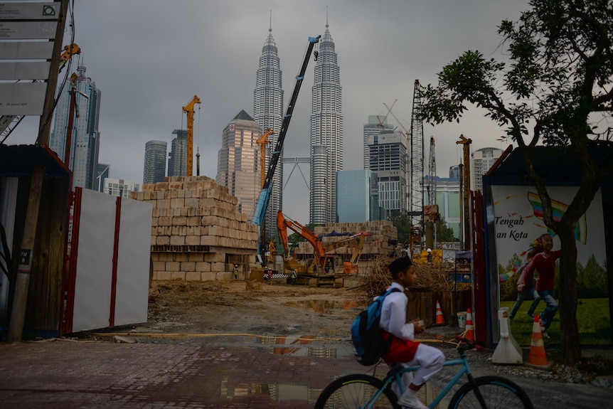A boy rides his bicycle in front of a construction site as Malaysia's iconic Petronas Twin Towers loom in the background.