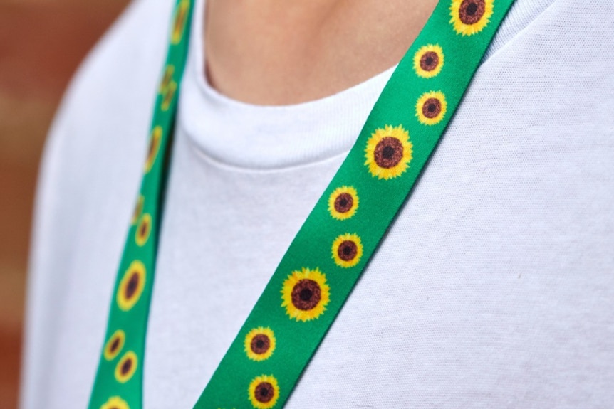 A person with a white t shirt wearing a bright green lanyard with sunflowers on it