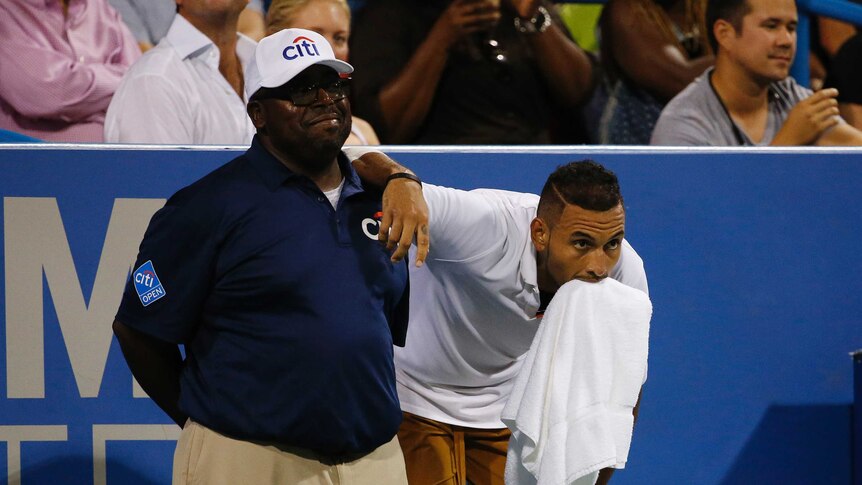 Nick Kyrgios, with a towel in his mouth, leans on the shoulder of a smiling linesman.
