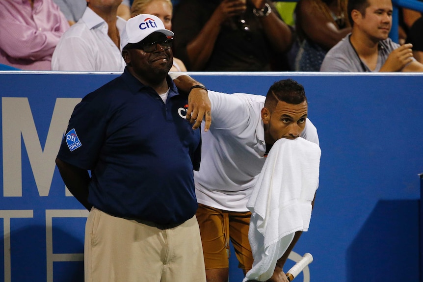 Nick Kyrgios, with a towel in his mouth, leans on the shoulder of a smiling linesman.