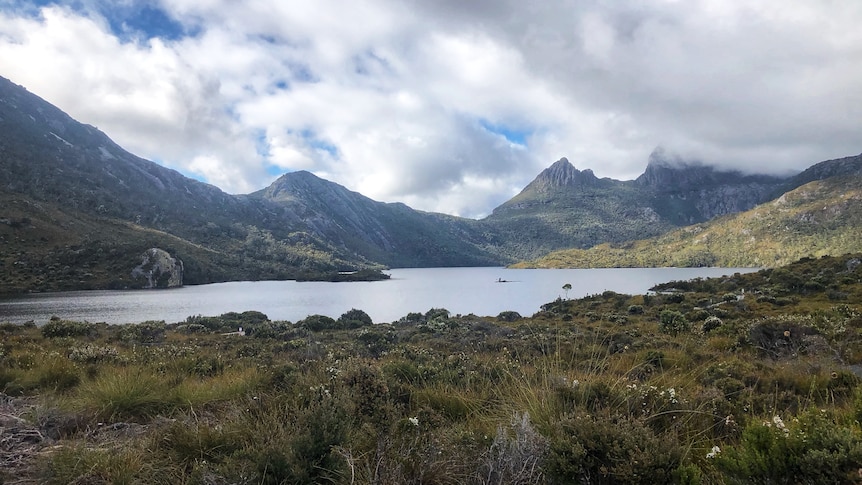 Cradle Mountain stretches up behind Dove Lake, with clouds partially obscuring its peak.