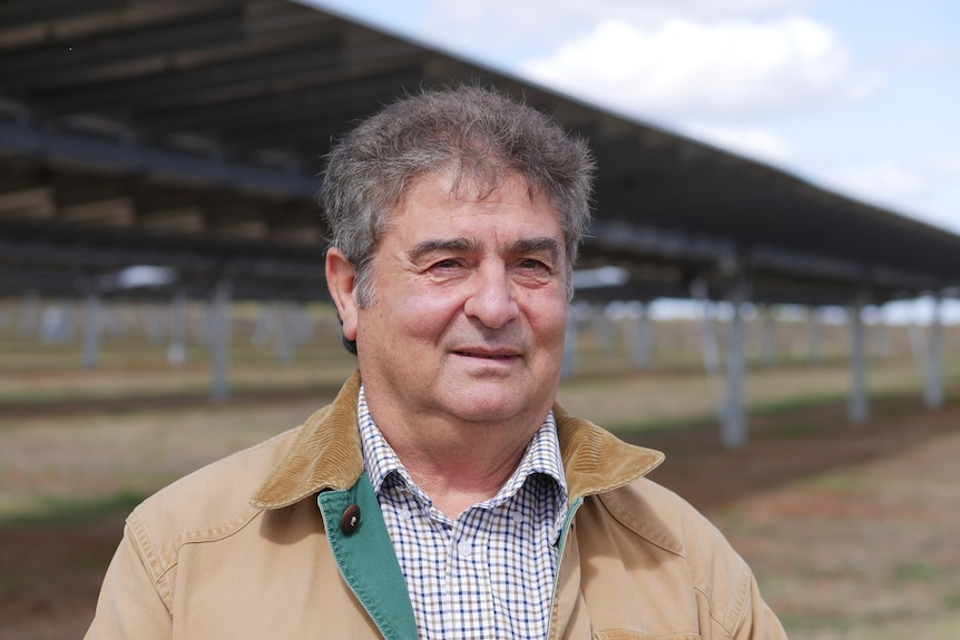 A man smiles slightly at the camera with solar panels in the background.