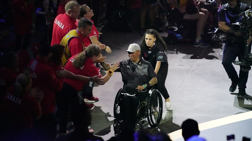 George Nepata sits in a wheelchair as he clasps the hand of members of the Canadian team, in celebration.