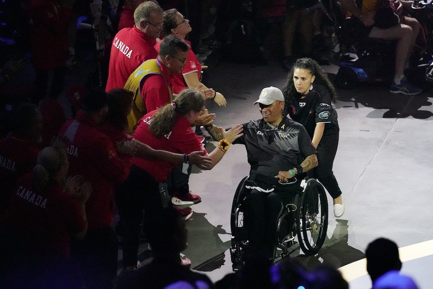 George Nepata sits in a wheelchair as he clasps the hand of members of the Canadian team, in celebration.